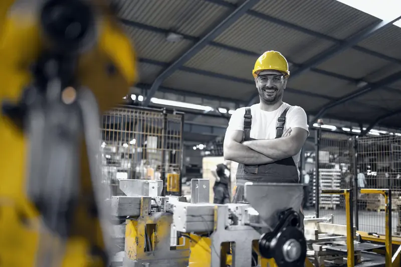 Operador de planta con los brazos cruzados junto a una máquina industrial